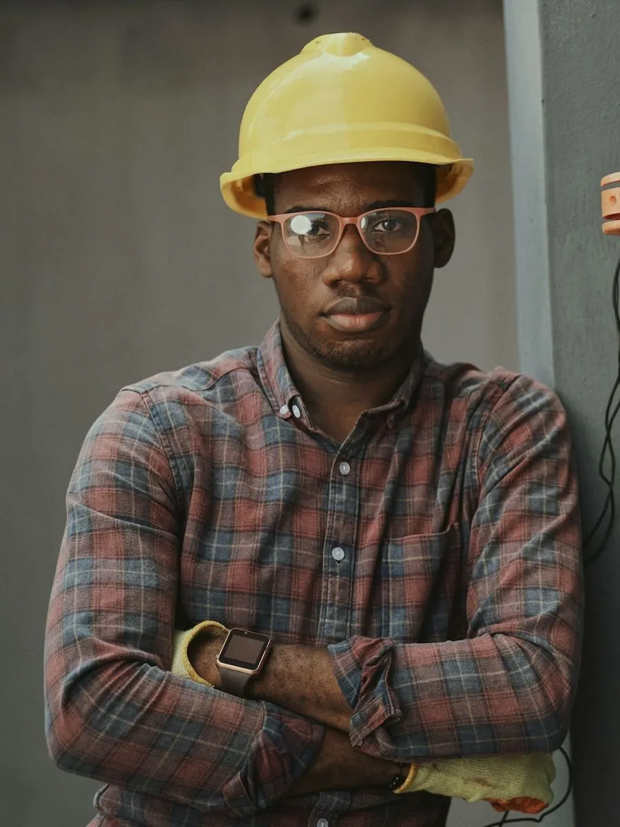 Tradesman in a plaid shirt and yellow hard hat beside an electrical meter