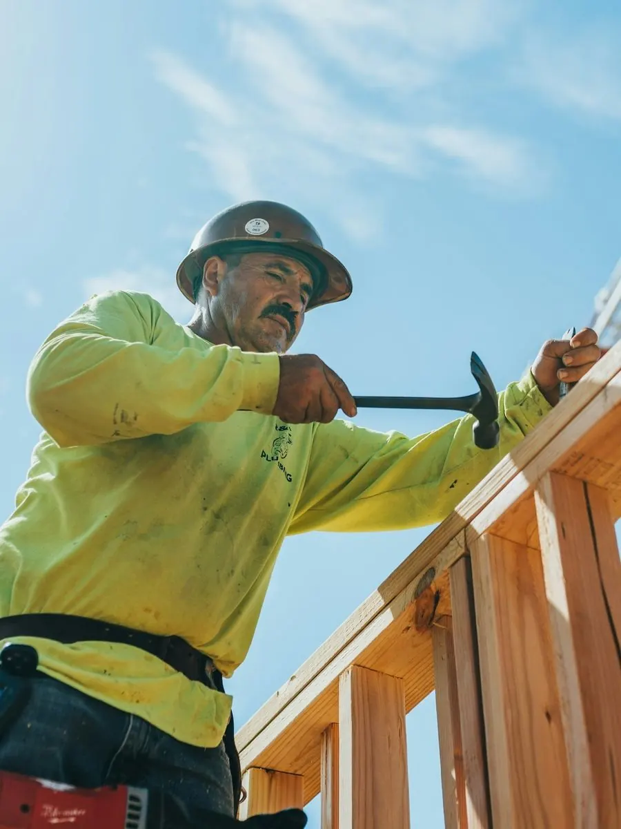 Framer driving a nail into a new stud wall against a blue sky