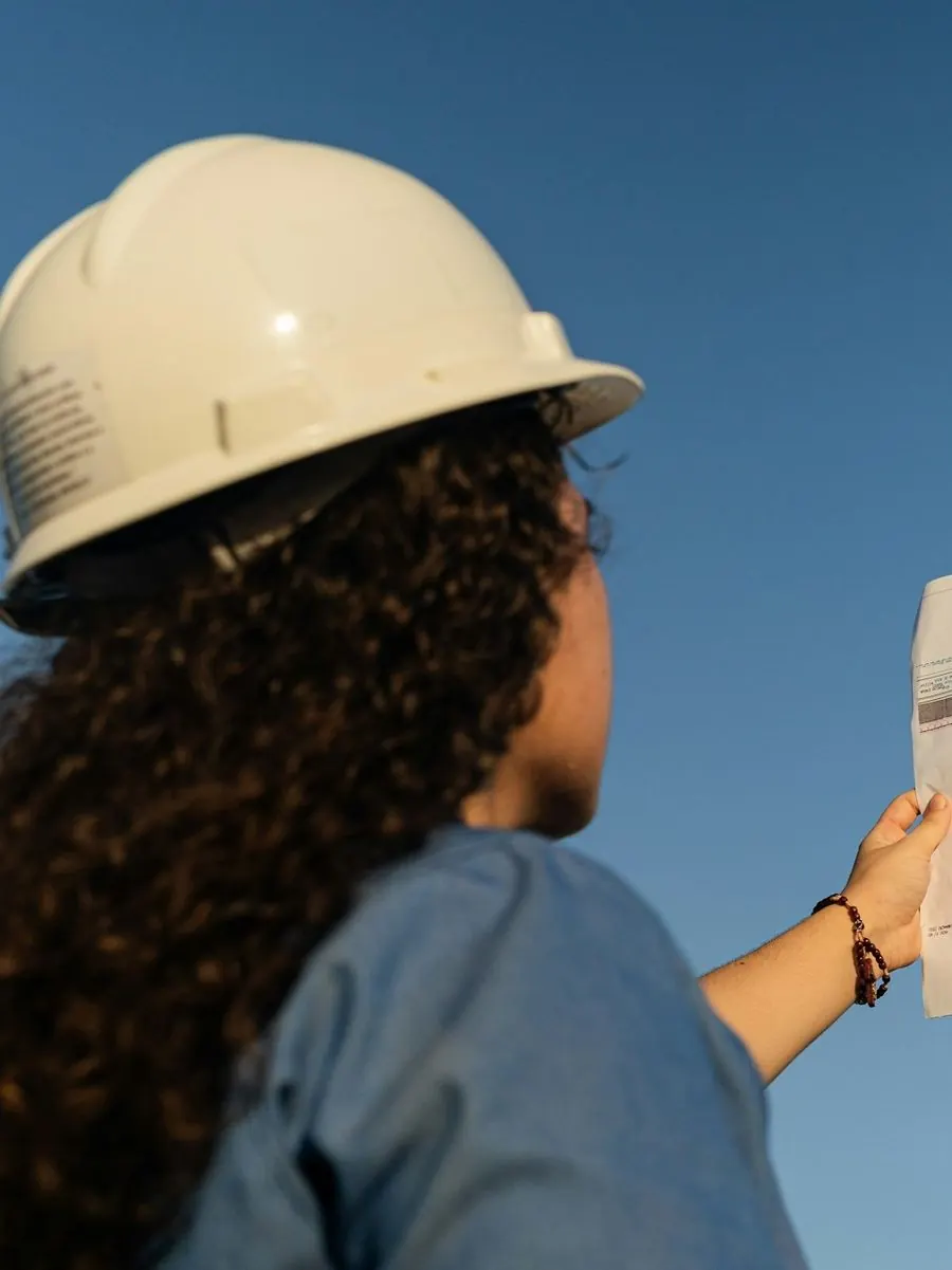 Engineer in a hard hat holding up a sheet of construction drawings