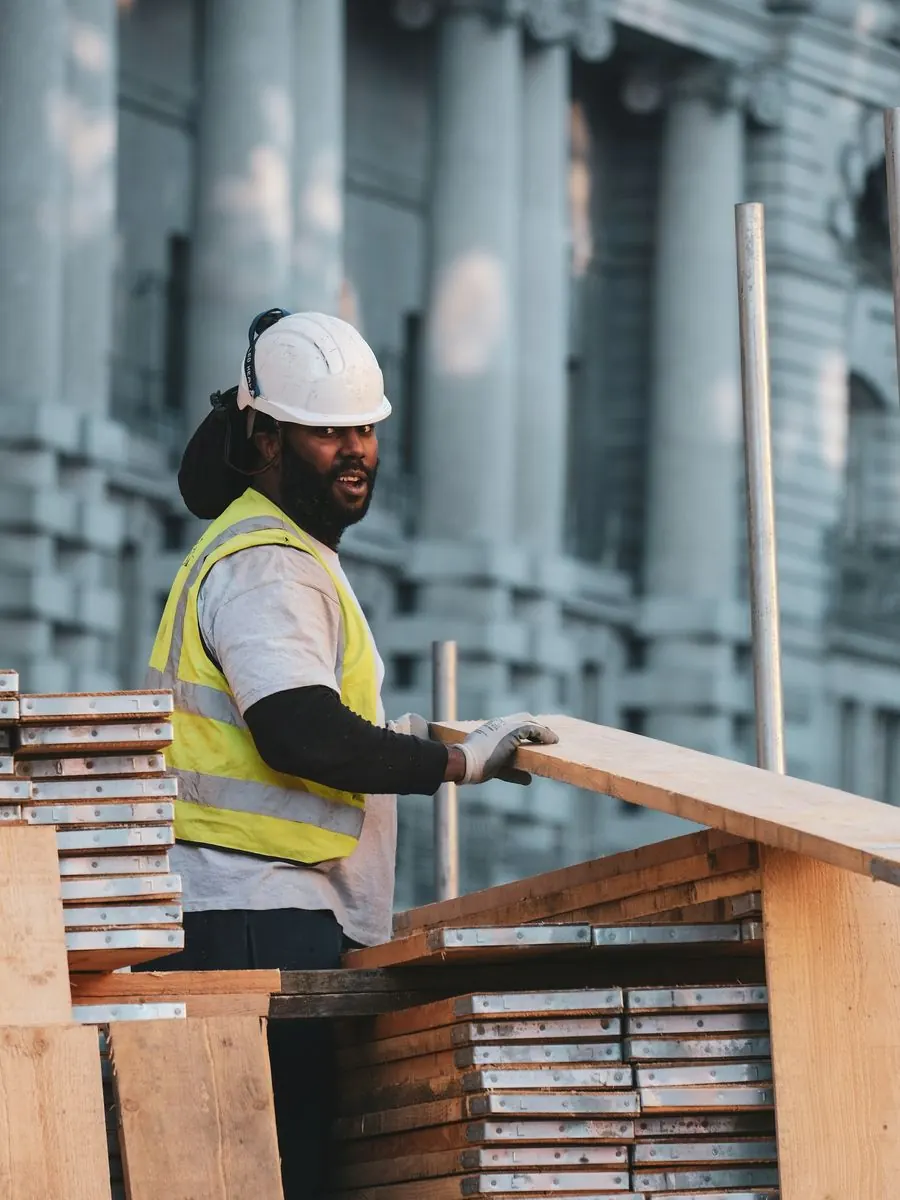 Carpenter in a hi-vis vest stacking lumber in front of a historic stone building