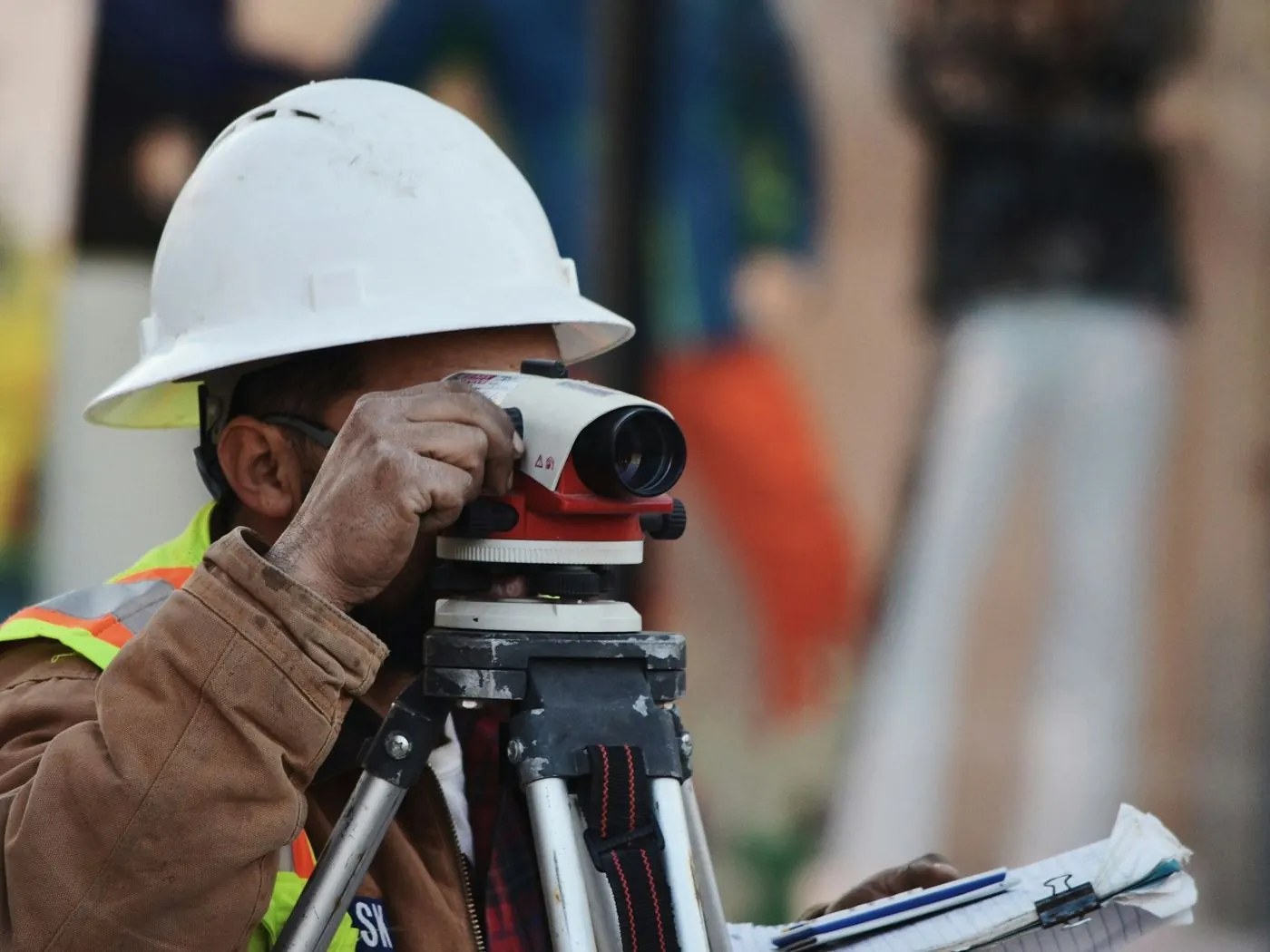 Surveyor in a white hard hat sighting through an optical level on a city job